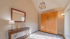 Ein Flur mit einem Holztischchen, einem Spiegel, einem geometrischen Lichtarmaturen und einem Holzschrank.