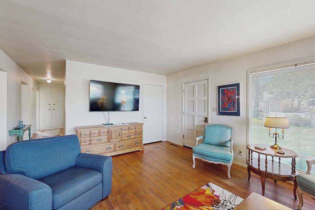 A living room with a blue sofa, a wooden cabinet, a television, and a window with blinds.