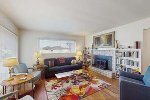 A living room with a sofa, coffee table, and fireplace, with a bookshelf and window in the background. - West End Wanderlust - Stylish Coastal Escape (Eureka)