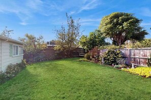 A residential backyard with a well-maintained lawn, a wooden fence, and various plants. - West End Wanderlust - Stylish Coastal Escape (Eureka)