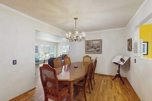 A dining area with a wooden table and chairs, a chandelier, and a painting on the wall. - West End Wanderlust - Stylish Coastal Escape (Eureka)