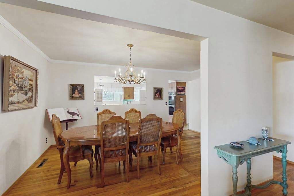 A dining area with a wooden table and chairs, a chandelier, and framed pictures on the walls.