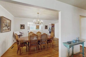 A dining area with a wooden table and chairs, a chandelier, and framed pictures on the walls. - West End Wanderlust - Stylish Coastal Escape (Eureka)
