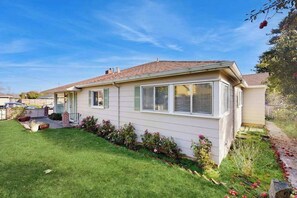 A single-story house with a front porch, a small garden with flowers, and a clear blue sky. - West End Wanderlust - Stylish Coastal Escape (Eureka)