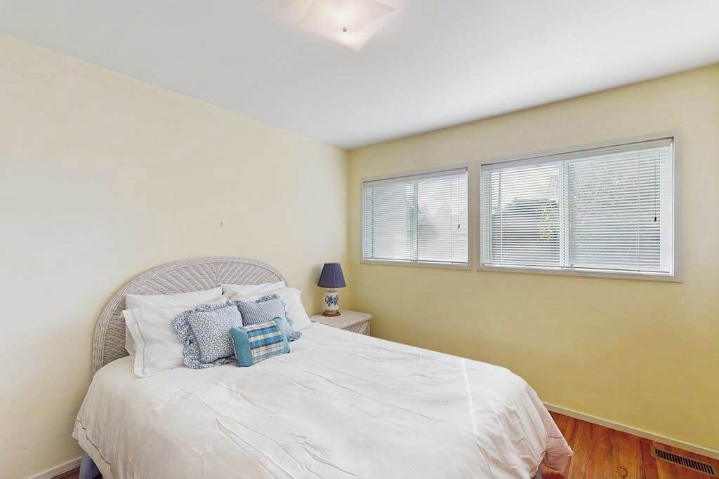 A bedroom with a bed, a nightstand, a lamp, and two windows with blinds.