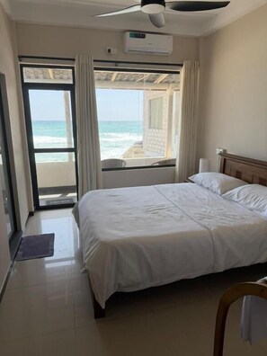 A hotel room with a bed, a ceiling fan, an air conditioning unit, and a view of the ocean through a sliding door. - Pelican Ahangama (Ahangama)