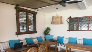 Um quarto com uma mesa de jantar de madeira, cadeiras de vime, um sofá com almofadas azuis e um lustre.