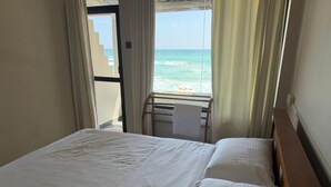 Quarto de hotel com cama, janela com cortinas e vista para a praia.