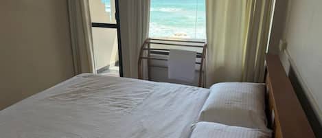 A hotel room with a bed, a window with curtains, and a view of the beach.