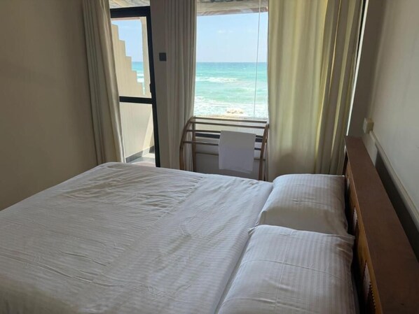 Una habitación de hotel con cama, ventana con cortinas y vista a la playa.