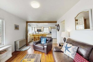 Ein Wohnzimmer mit einer Ledersofa, einem Couchtisch und einem Essbereich mit Holzsesseln.