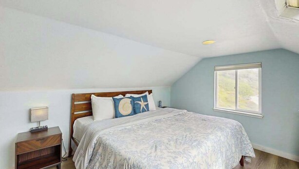 A bedroom with a bed, nightstand, and window. - Seascape Home - Spacious Coastal Retreat with Ocean Views (Trinidad)