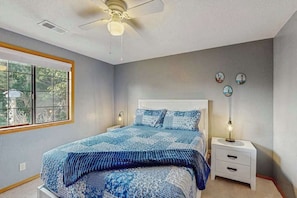 A bedroom with a bed, a ceiling fan, a nightstand, and a window.