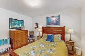 Ein Schlafzimmer mit einem Bett, einem Holzkasten, zwei Stühlen, einem Fernseher und gerahmten Kunstwerken an den Wänden.