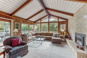 Ein geräumiges Wohnzimmer mit hoher Decke, großen Fenstern, einem Kamin und einer Steinwand.