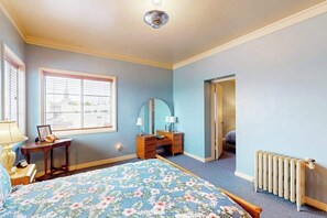 Ein Schlafzimmer mit Bett, Kommode, Spiegel, Fenster und Heizkörper.