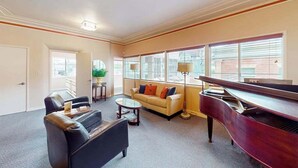 A living room with a piano, sofa, coffee table, and a view through large windows. - Eureka Theater Apartment (Eureka)