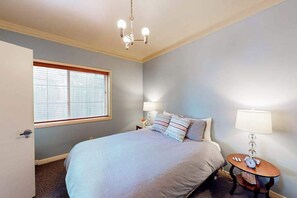 A bedroom with a bed, bedside lamps, a small table with a clock, and a window with blinds. - Eureka Theater Apartment (Eureka)