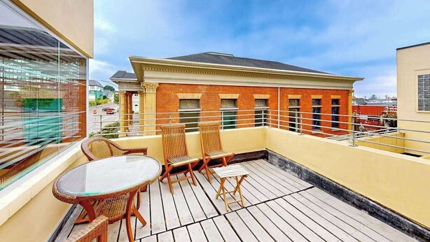 A rooftop terrace with a glass table and chairs, a brick building in the background, and a clear sky. - Eureka Theater Apartment (Eureka)