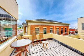 A rooftop terrace with a glass table and chairs, a brick building in the background, and a clear sky. - Eureka Theater Apartment (Eureka)