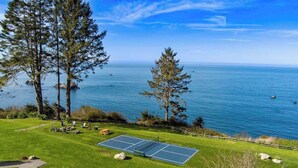 A tennis court with a scenic ocean view, surrounded by grass and trees. - The Trinidad Pearl - Oceanfront Home & Hot Tub (Trinidad)