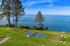 A tennis court with a scenic ocean view, surrounded by grass and trees. - The Trinidad Pearl - Oceanfront Home & Hot Tub (Trinidad)