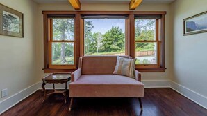 A room with a sofa, a small table, and large windows with a view of trees and a fence. - The Trinidad Pearl - Oceanfront Home & Hot Tub (Trinidad)