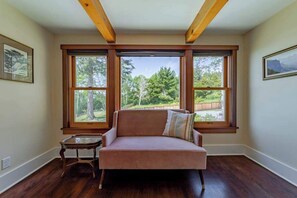 A room with a sofa, a small table, and large windows with a view of trees and a fence. - The Trinidad Pearl - Oceanfront Home & Hot Tub (Trinidad)