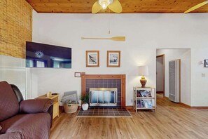 Un salon avec une cheminée, un téléviseur fixé au mur et un plafond en bois.