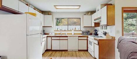 A compact kitchen with white cabinets, a central island, and a window overlooking a natural landscape.
