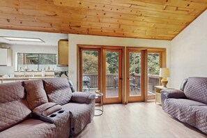 Una habitación con techo de madera, una puerta corrediza de vidrio que da a una terraza exterior y dos sofás.