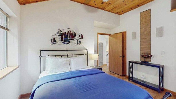 Un dormitorio con una cama, techo de madera, una obra de arte en la pared, una mesita de noche y una puerta.