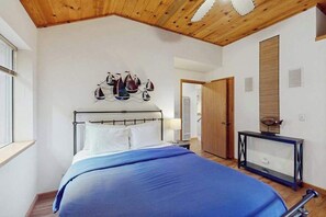 A bedroom with a bed, a wooden ceiling, a wall-mounted artwork, a bedside table, and a door.