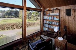 A cozy reading nook with a large window, a bookshelf, and a comfortable chair. - Ocean Treasures: Retro Home, 4 Min Walk to Beach (Smith River)