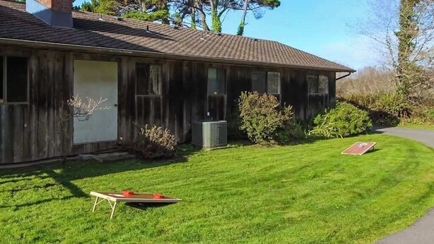 A single-story building with a sloped roof, a front door, and a small front yard with a lawn and a single red object. - Ocean Treasures - Charming Coastal Home Near the Beach (Smith River)