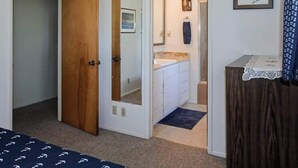 A bedroom with a wooden door, a bathroom with a sink and mirror, and a small table with a lace tablecloth. - Ocean Treasures - Charming Coastal Home Near the Beach (Smith River)