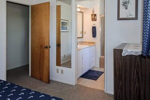A bedroom with a wooden door, a bathroom with a sink and mirror, and a small table with a lace tablecloth. - Ocean Treasures - Charming Coastal Home Near the Beach (Smith River)