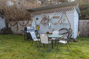 A backyard with a barbecue grill, a table with chairs, and a covered area with a lattice fence. - Ocean Treasures - Charming Coastal Home Near the Beach (Smith River)