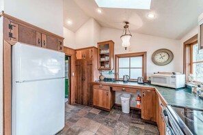 A kitchen with wooden cabinets, a white refrigerator, a microwave, and a window. - Seaside Meadow - Peaceful Coastal Retreat Surrounded by Nature (Trinidad)