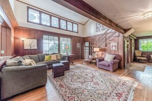 A spacious living room with a large window, a staircase, and a cozy seating area. - Seaside Meadow - Peaceful Coastal Retreat Surrounded by Nature (Trinidad)