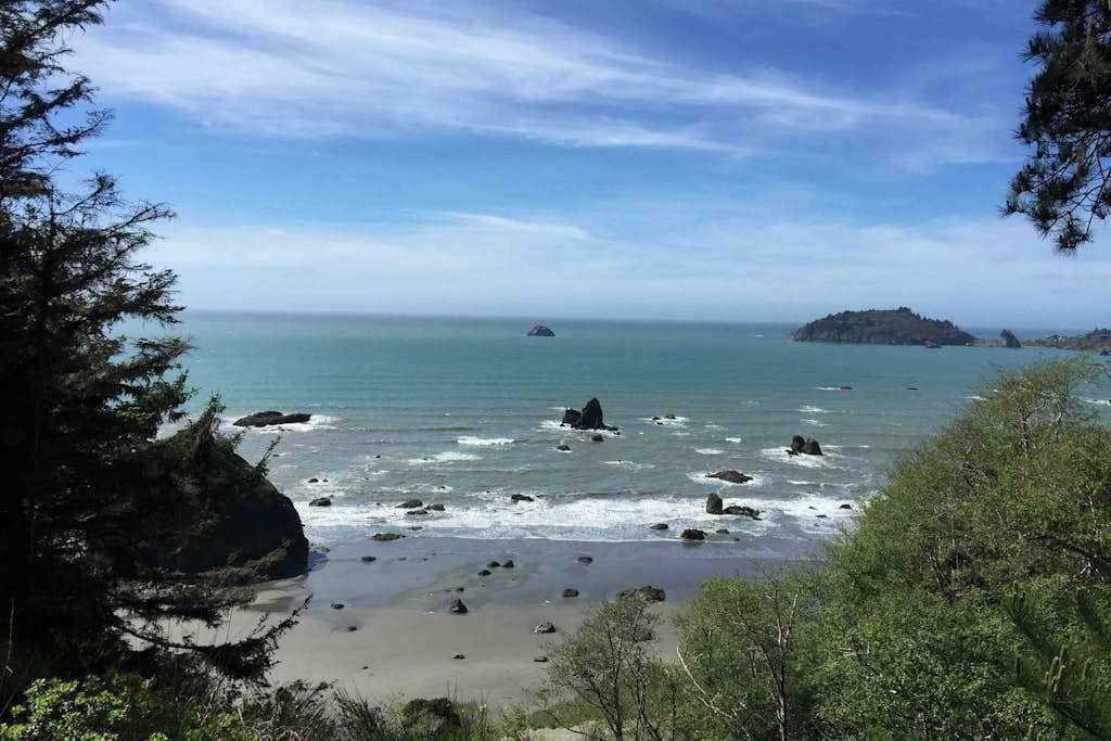 A coastal landscape with a beach, rocky outcrops, and a distant island.