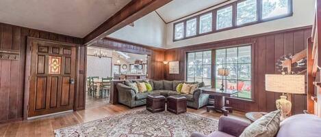 A spacious living room with a large sectional sofa, a patterned rug, and a dining area visible through an open door.