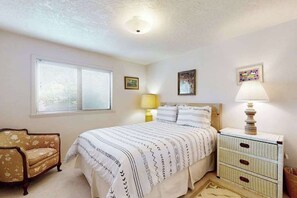 A bedroom with a bed, bedside tables, a chair, and a window with blinds. - Humboldt Bay Retreat (Eureka)