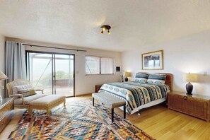 Ein Schlafzimmer mit einem Bett, einer Bank, einem Nachttisch, einer Lampe, einem Fenster mit Jalousien und einer Deckenleuchte.