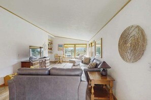 A living room with a sofa, a television, a table, and a decorative wall piece. - Pacific View Escape - Bay Views & Jetted Tub (Loleta)