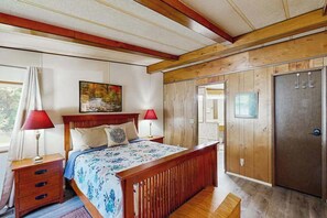 Un dormitorio con cama de madera, dos mesitas de noche, un tocador, un banco, una puerta y una ventana.