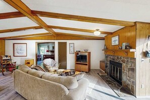 Una sala de estar con chimenea, vigas de madera, un sofá y un televisor.