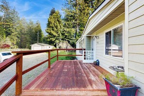 A wooden deck with a railing, a house with a garage, and a clear sky. - Redwood Coast River House (Crescent City)