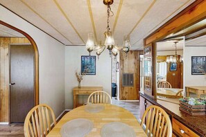 A dining area with a wooden table and chairs, a chandelier, and a large mirror reflecting the room. - Redwood Coast River House (Crescent City)