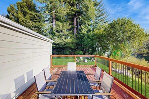 A deck with a table and chairs, surrounded by a wooden railing, overlooking a grassy area with trees. - Redwood Coast River House (Crescent City)